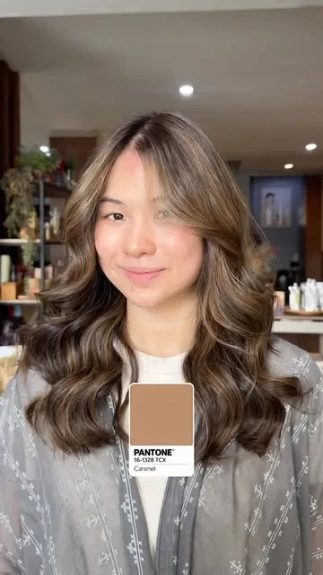 A woman facing the camera with long caramel balayage waves.